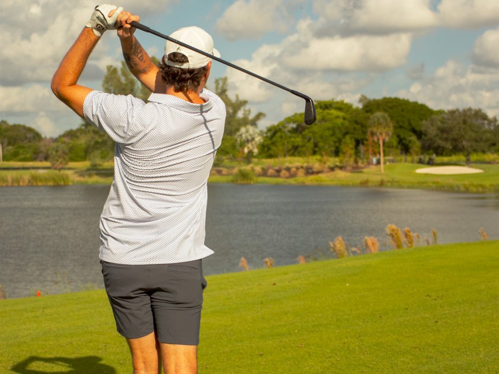 A golfer's follow-through with a lake fronting the green at Pompano Beach Golf Course